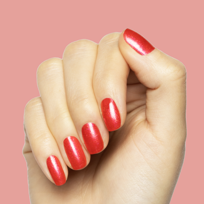 Hand with shiny bright pinky-red nails featuring Rodeo Queen polish for a vibrant at-home manicure look