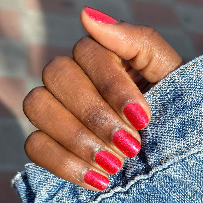 Close-up of hand with short nails painted bright pinky-red silver shimmer using Rodeo Queen polish for at home mani