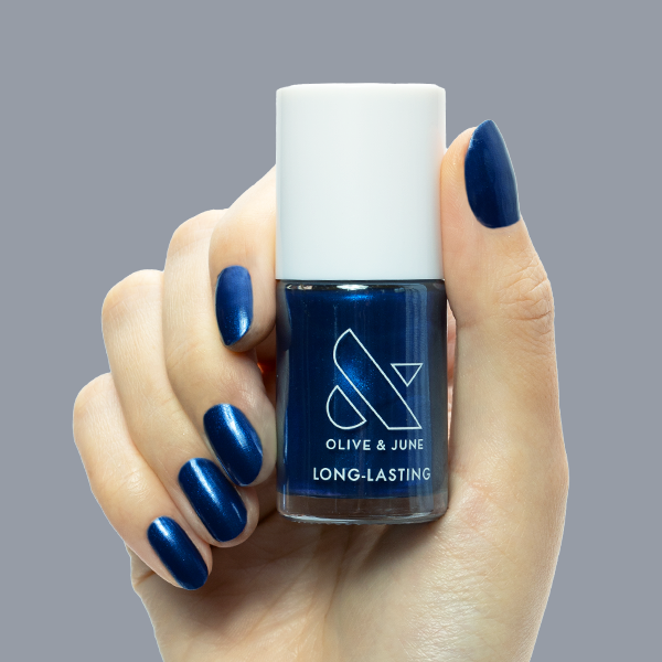 Hand holding Olive and June Sapphire Season nail polish with deep sapphire blue gel polish manicure and chrome finish