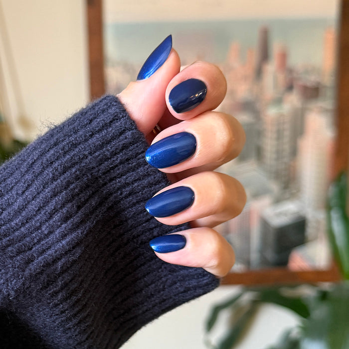 Hand with long almond nails painted in Sapphire Season ultra shimmery chrome deep blue gel polish manicure