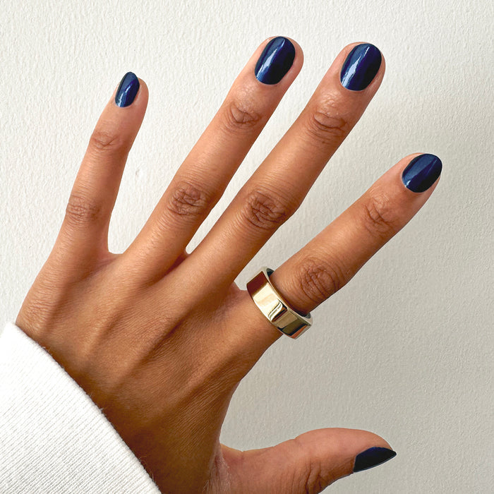 Hand with short rounded nails coated in Sapphire Season deep blue gel polish showing smooth shiny mani finish