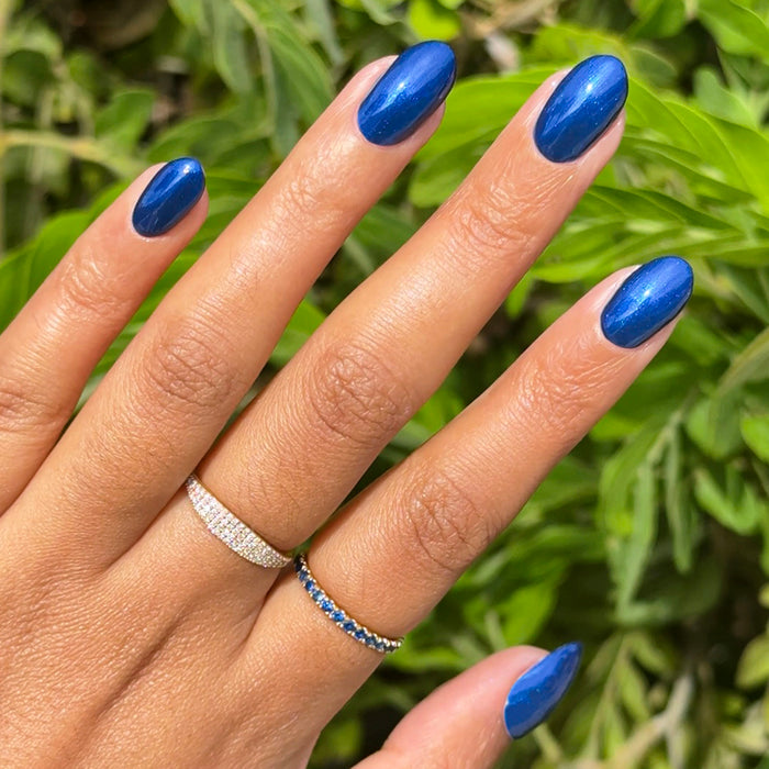 Hand with oval nails polished in Sapphire Season showing vibrant deep blue gel polish with shiny chrome manicure finish outdoors