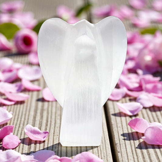White selenite angel sculpture on a wooden surface with pink flower petals