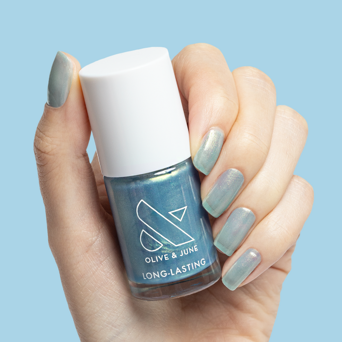 Sequin Everything blue iridescent long-lasting nail polish bottle held with matching mani on light blue background