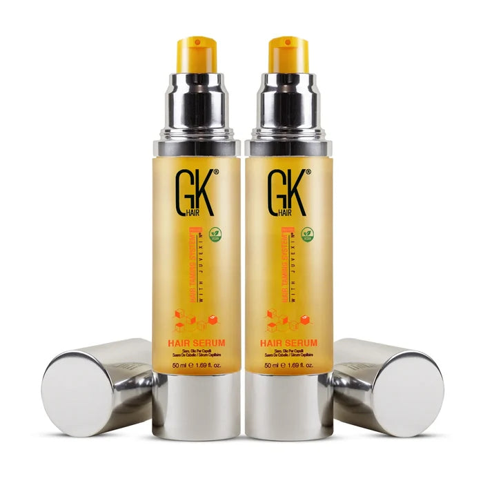 Two GK Hair Argan Oil Serum 50 ml bottles standing with pumps exposed, their silver caps lying on either side