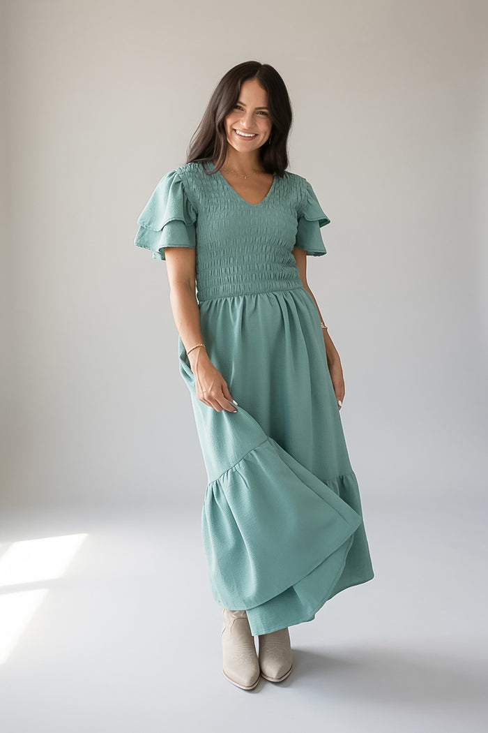 A woman wearing a sage green tiered maxi dress with ruffled short sleeves and smocked detailing