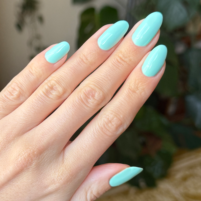 Hand with neatly shaped nails painted in vibrant true turquoise using Slam Dunk gel polish for an elegant mani
