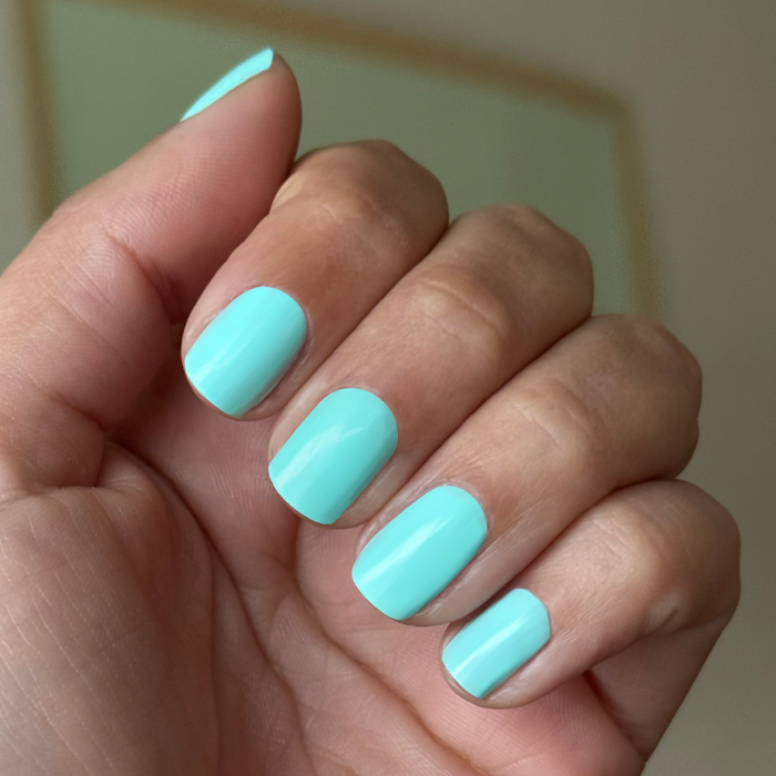 Hand with short nails polished in bright true turquoise using Slam Dunk gel polish for a fresh at-home mani