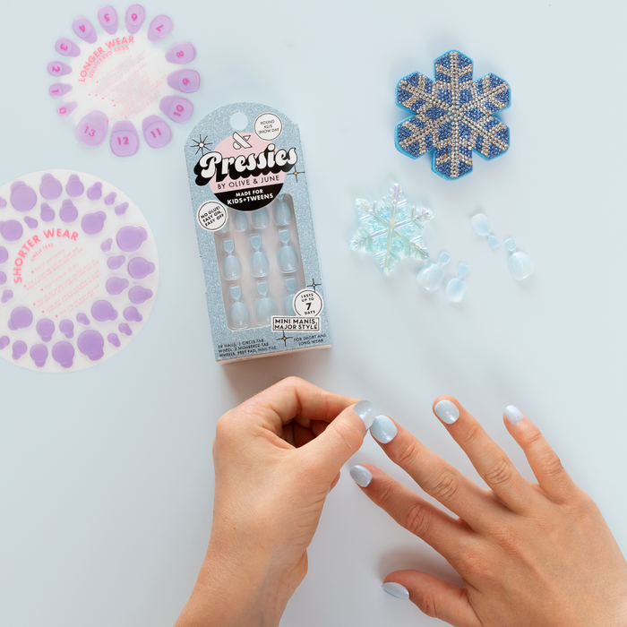 Snow Day - Pressies | Extra Short Short | Round showing pale blue press-on nails being applied with snowflake decor nearby