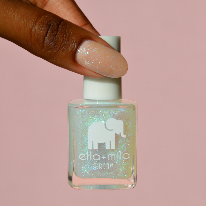 Spin Me Round iridescent shimmer nail polish on a deep skin tone, holding the bottle on a pink background