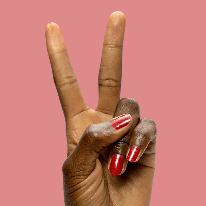Hand with Splash of Cran gel polish in shimmering pinky-red on short nails against a soft coral background
