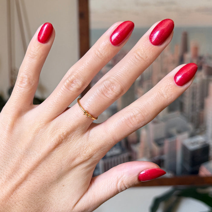 Hand with long nails painted in shimmering pinky-red gel polish Splash of Cran against a blurred city background