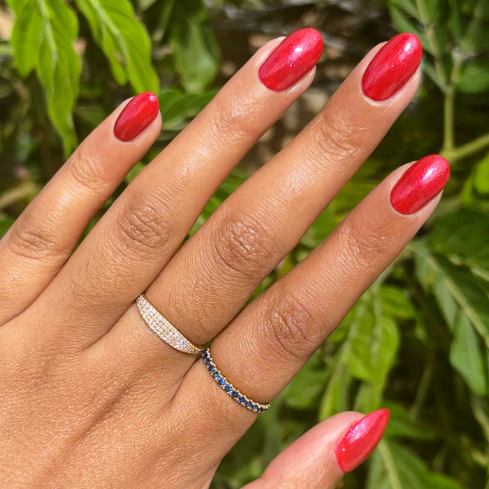 Hand with medium-length nails painted in shimmery pinky-red gel polish Splash of Cran against leafy green background