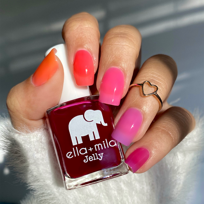 Spread the Love orange with pink and magenta jelly mix-and-match manicure, holding a bottle