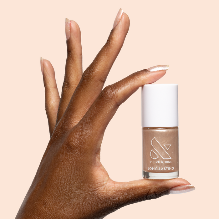 Hand with warm champagne shimmer nails holding Starfruit Shimmer Gloss nail polish bottle against soft peach background