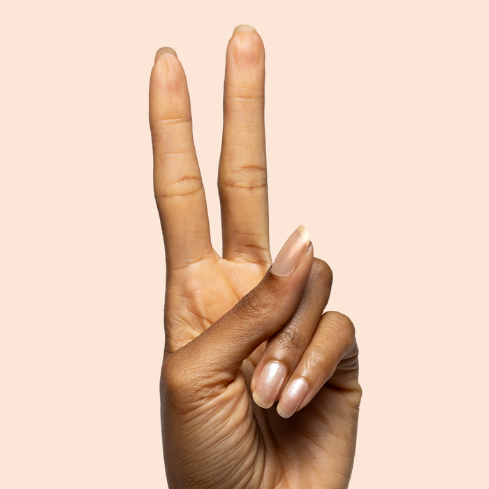 Hand with natural almond nails painted in warm champagne using Starfruit Shimmer Gloss polish on soft peach background
