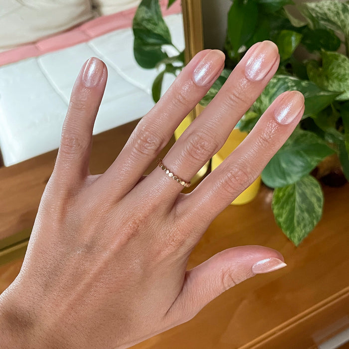 Hand with medium natural nails coated in warm champagne shimmer using Starfruit Shimmer Gloss against indoor background