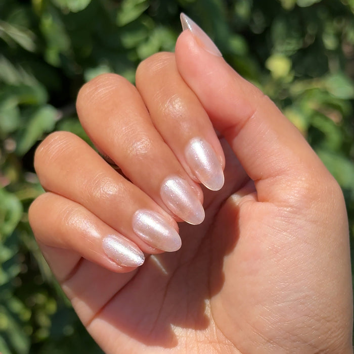 Hand with almond-shaped nails coated in glossy Starfruit Shimmer Gloss polish outdoors with natural greenery background