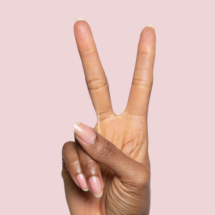 Hand with natural nails showing subtle shine and peace sign posed against a pink background with Starshower polish nearby
