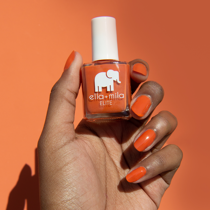 Sunset Escape burnt orange nail polish on a deep skin tone against an orange background