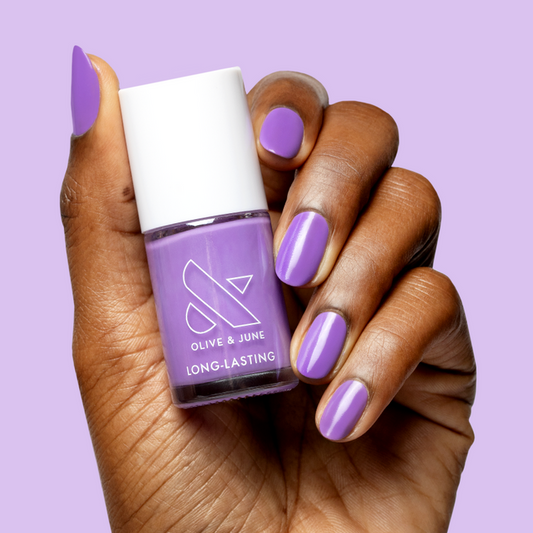 Hand holding a bottle of Tennis Skirt nail polish by Olive and June with matching purple polished nails