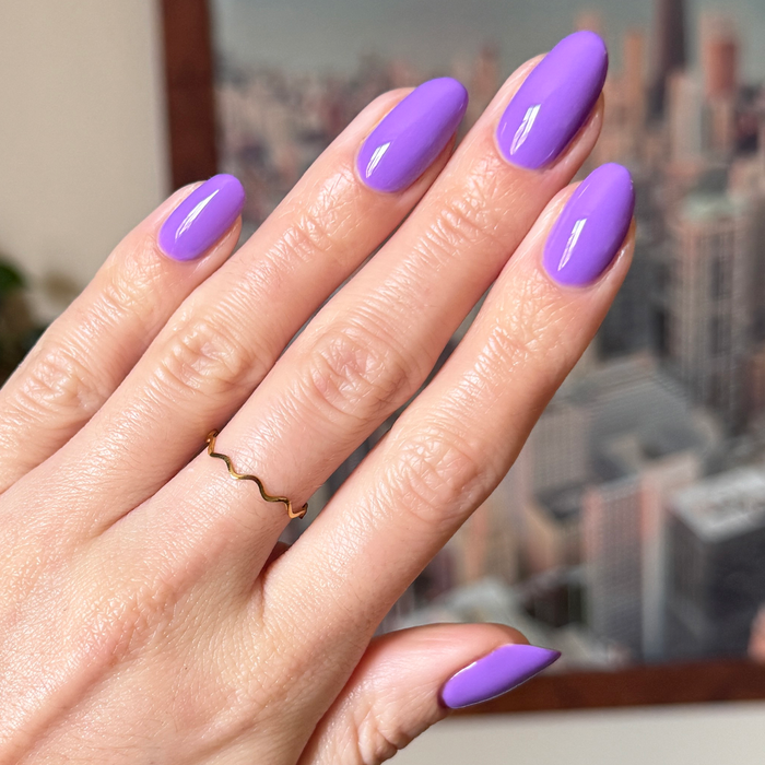 Hand with smooth nails painted bright purple Tennis Skirt polish for a glossy, long-lasting at-home mani by Olive and June