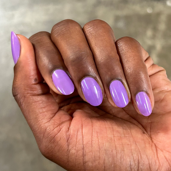 Hand with oval nails painted in bright purple Tennis Skirt polish for a smooth, glossy at-home manicure look