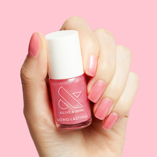 Hand holding That’s Amoray polish showing shiny sweet pink sheer manicure on nails against soft pink background