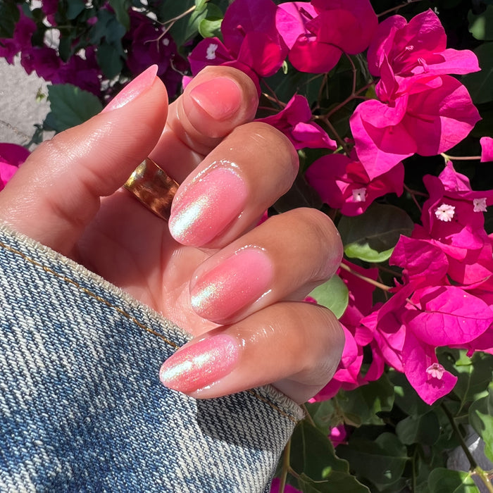 Hand with nails painted in iridescent sweet pink shiny manicure using That’s Amoray gel polish outdoors