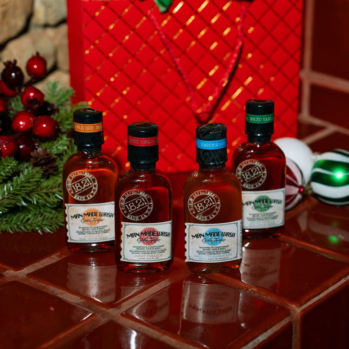 Four miniature bottles of Man Made Travel size wash on a tiled surface with Christmas decorations in the background.