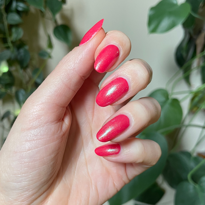 The Mermaid Effect Top Coat with iridescent pink shimmer and blue-green shift on vibrant red nails for a glossy mani
