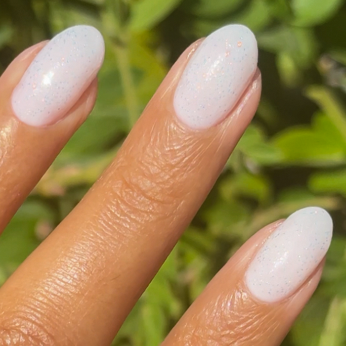 The Pixie Effect Top Coat adding a subtle iridescent shimmer over pastel polish for a delicate manicure look