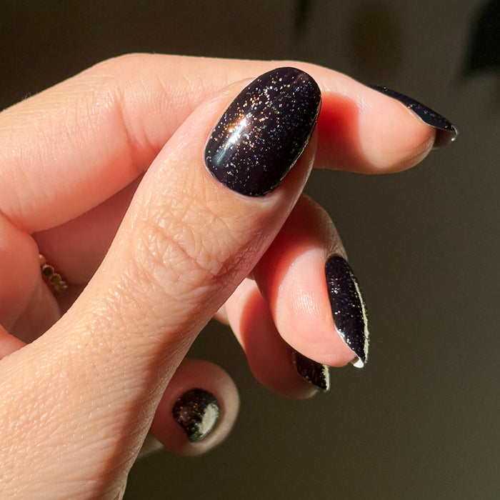 The Pixie Effect Top Coat adding sparkling iridescent shimmer over black polish for a dazzling manicure look