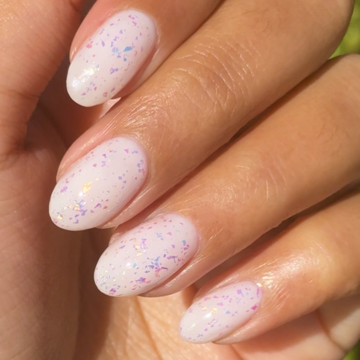 The Stardust Effect Top Coat with holographic flakes on soft white polish for a sparkling at home mani finish