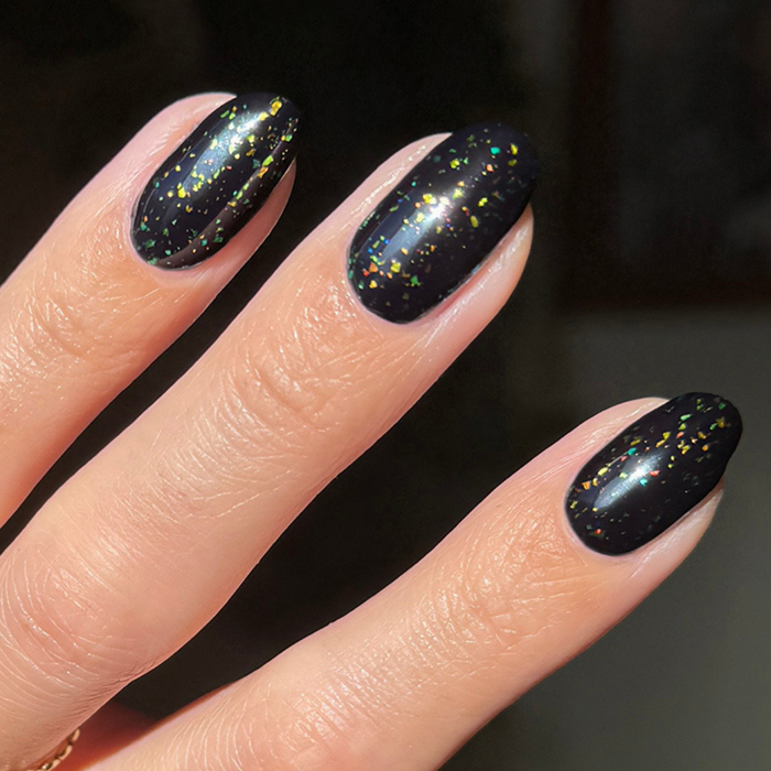 The Stardust Effect Top Coat on black polish displaying scattered holographic flakes for a vibrant manicure finish