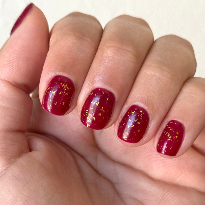 The Stardust Effect Top Coat adding reflective flake sparkle over glossy deep red polish for a bright manicure finish