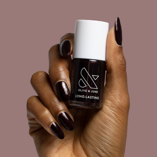 Hand holding Olive and June long-lasting nail polish in deep plum shade "To Me, You Are Perfect" for at-home mani use