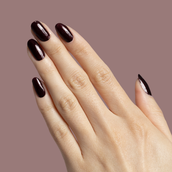 Hand showing nails polished with To Me, You Are Perfect deep plum metallic shimmer polish for at-home manicure.