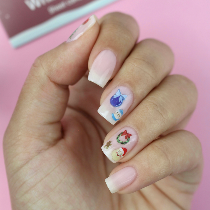 Whimsical Winter ornament and gingerbread decals on a sheer pink manicure with the packaging