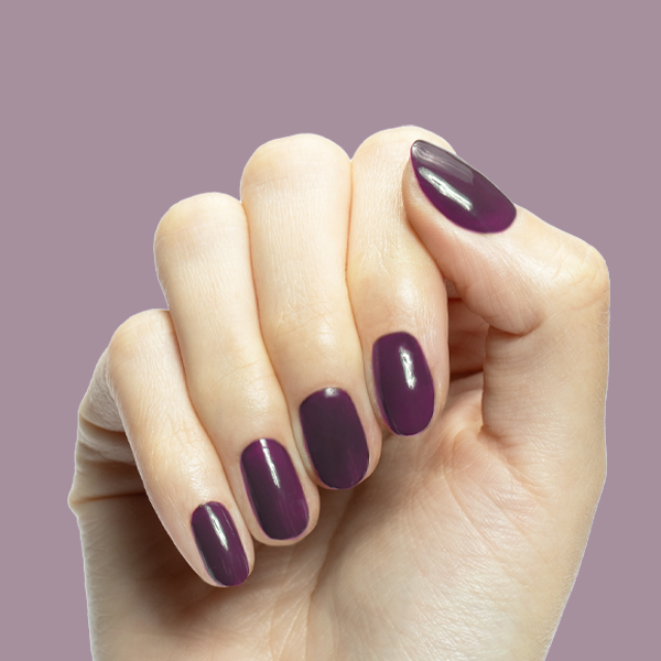 Hand with Who Likes Raisins? dark purple gel polish on medium rounded nails against soft muted purple background