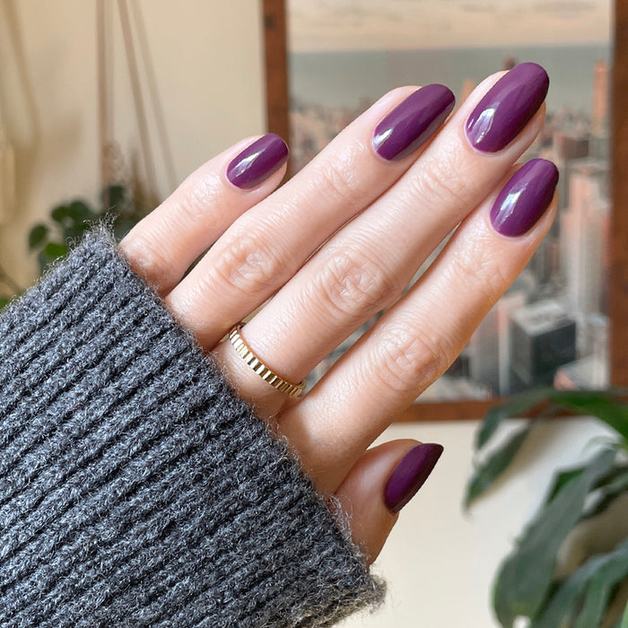 Hand with almond-shaped nails painted in Who Likes Raisins? gel polish holding a gray knit sleeve indoors