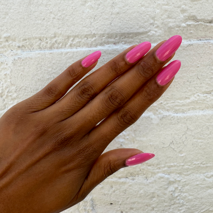 Hand with glossy bright peony pink gel polish manicure using Your Favorite Suit against light textured background