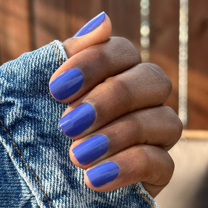 Hand with short nails painted in glossy bright denim blue Your Mani Looks So Good in Those Jeans polish